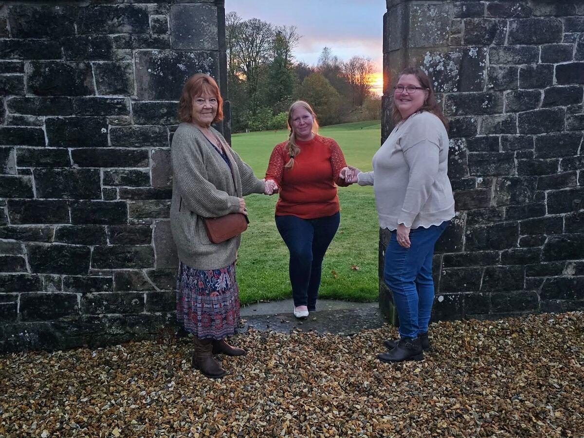 Three generations of the Twisted Chicks family holding hands beneath a stone archway at sunset